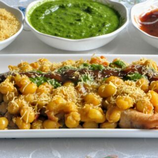 ragda samosa chaat in a plate with chutney and sev on the side.