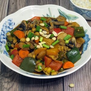 chickpea vegetable kung pao in a bowl served with rice in background.