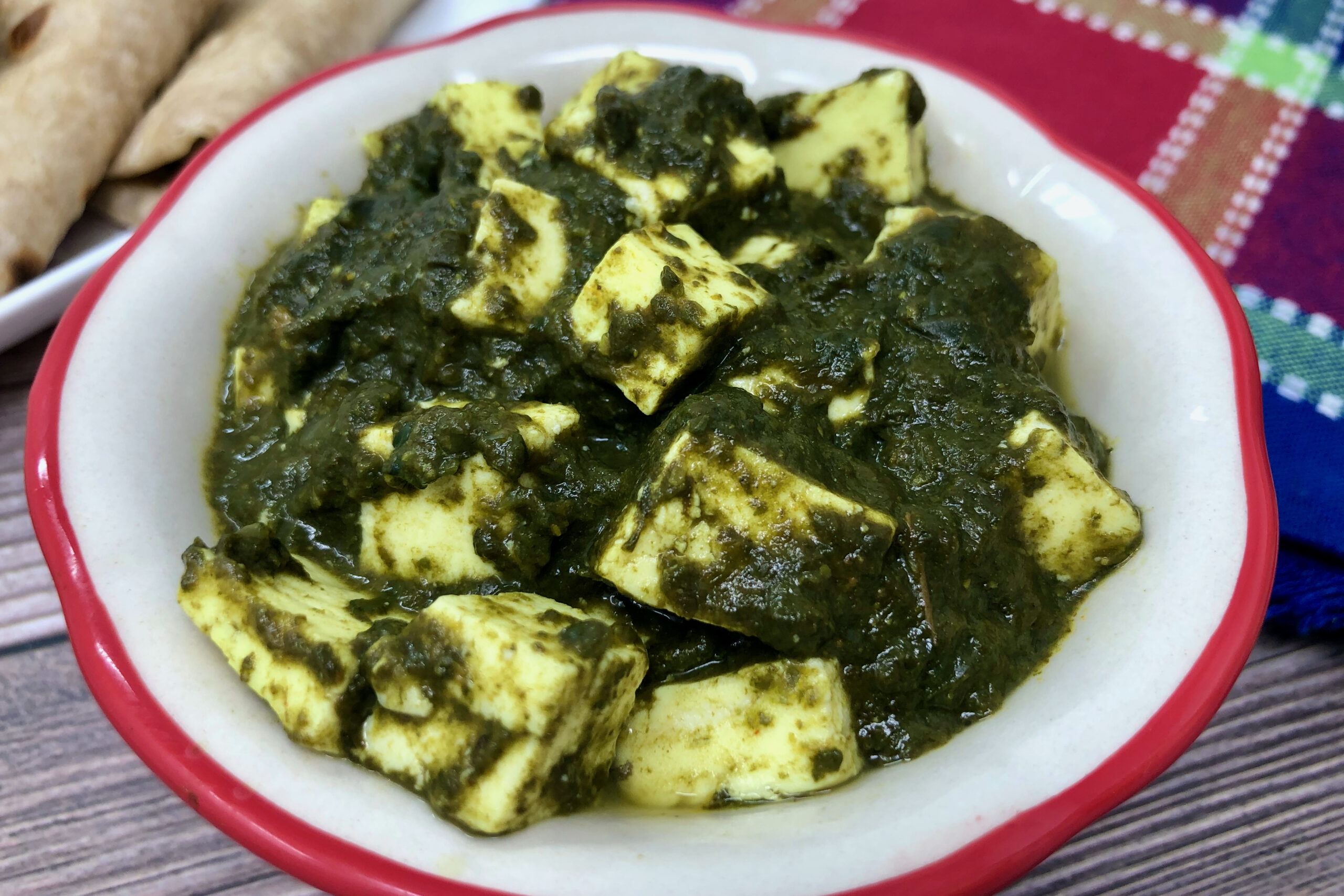 palak paneer in a bowl with roti in background.