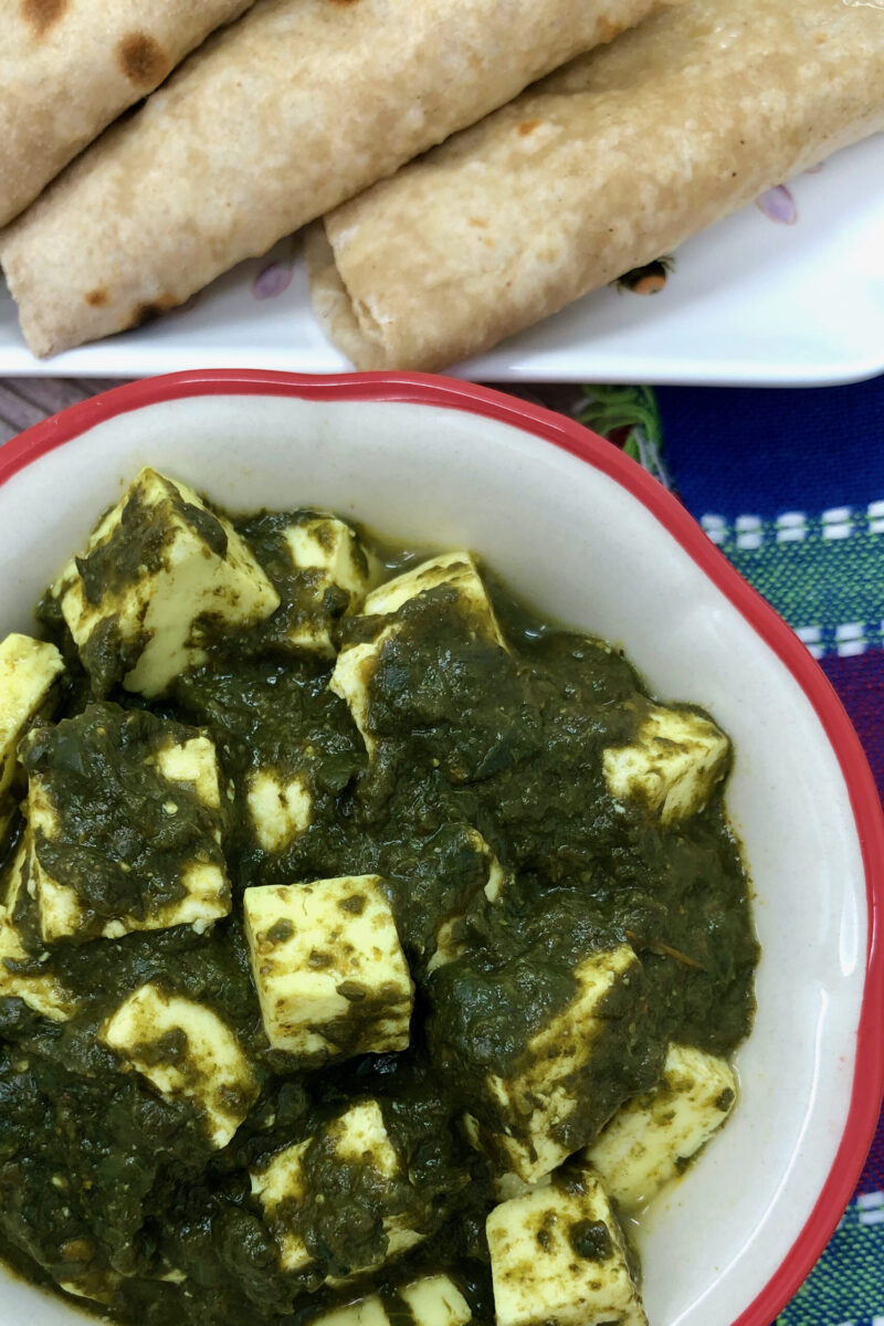paneer palak in a bowl with roti in background.