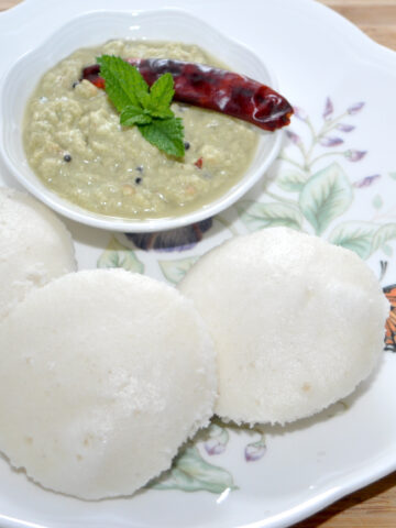 idli in a plate with sambar in background.