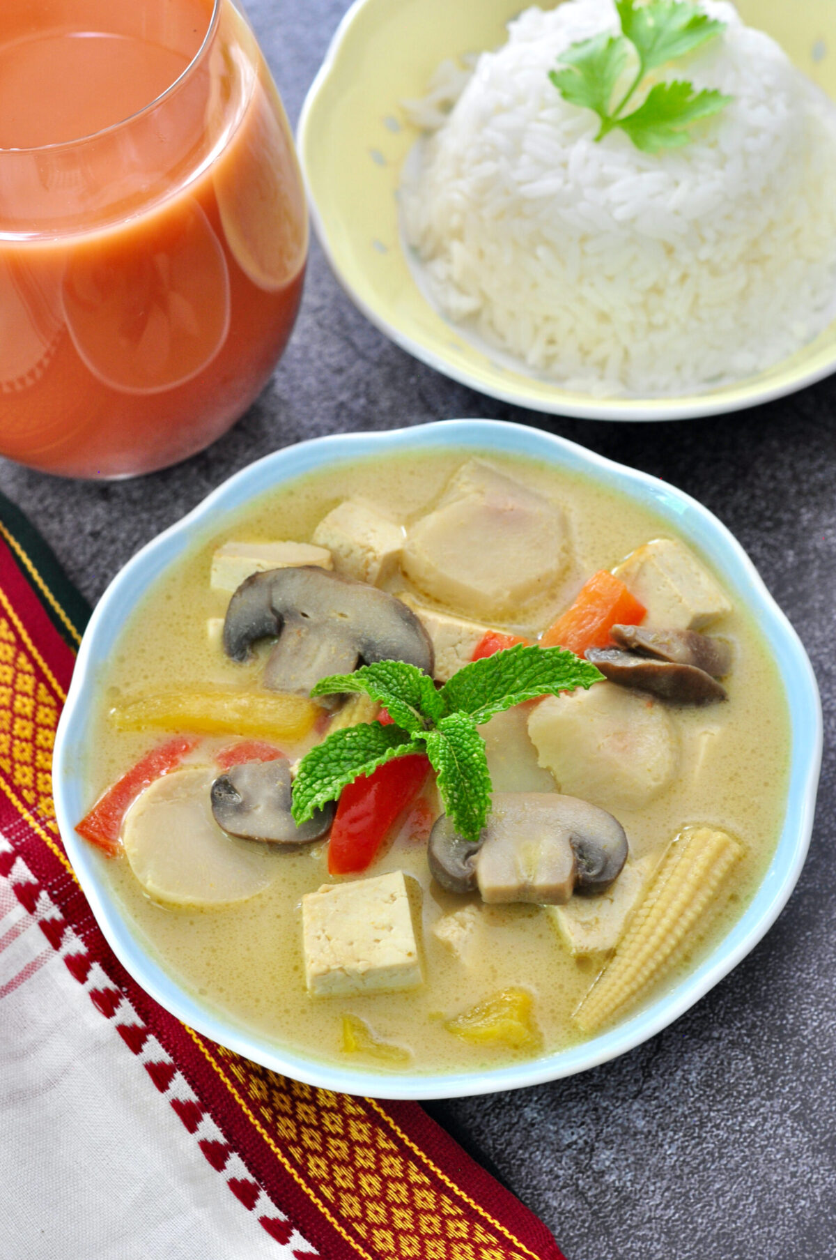 Thai green curry in a bowl with Thai tea and rice in background