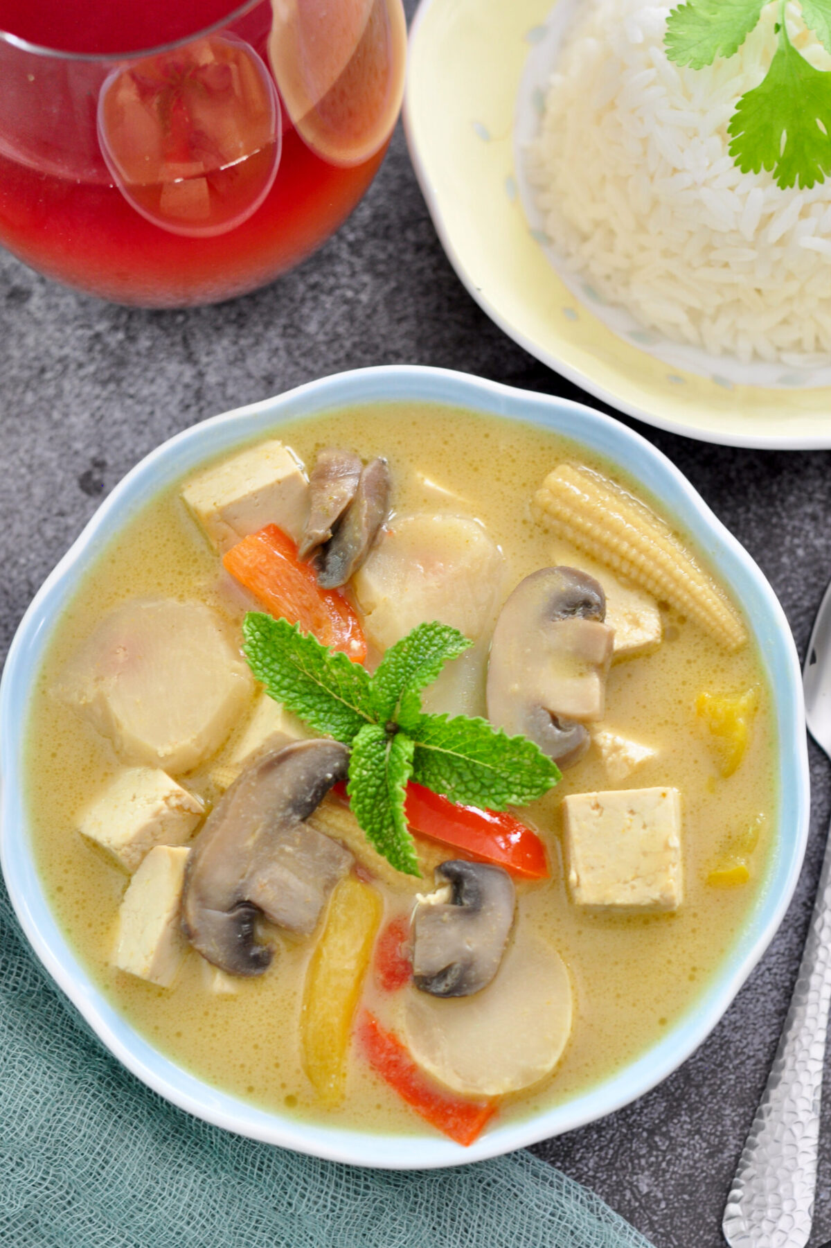 Thai green curry in a bowl with Thai tea and rice in background