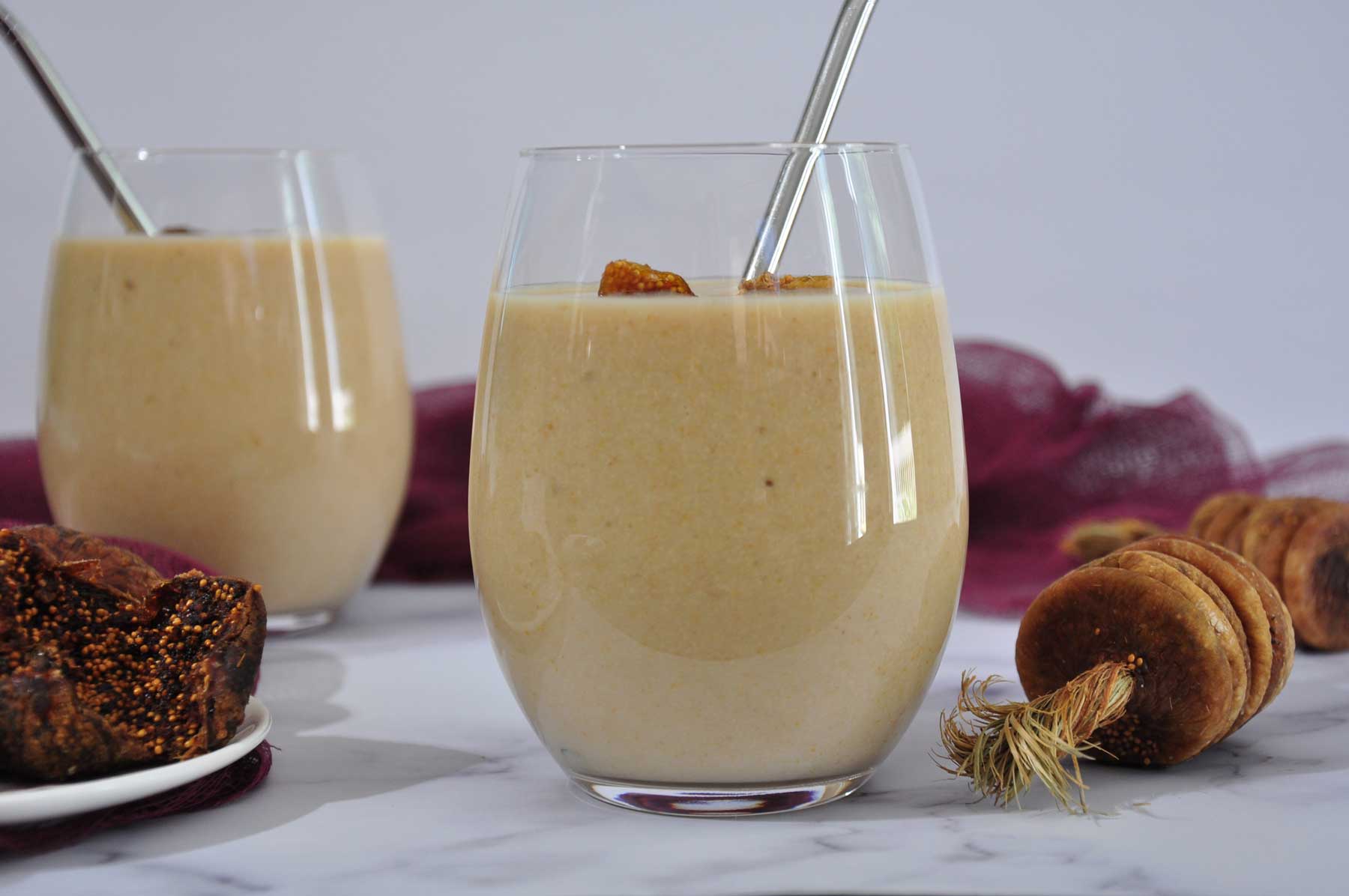 Fig smoothie in a glass with a steel straw and raw figs in the background.