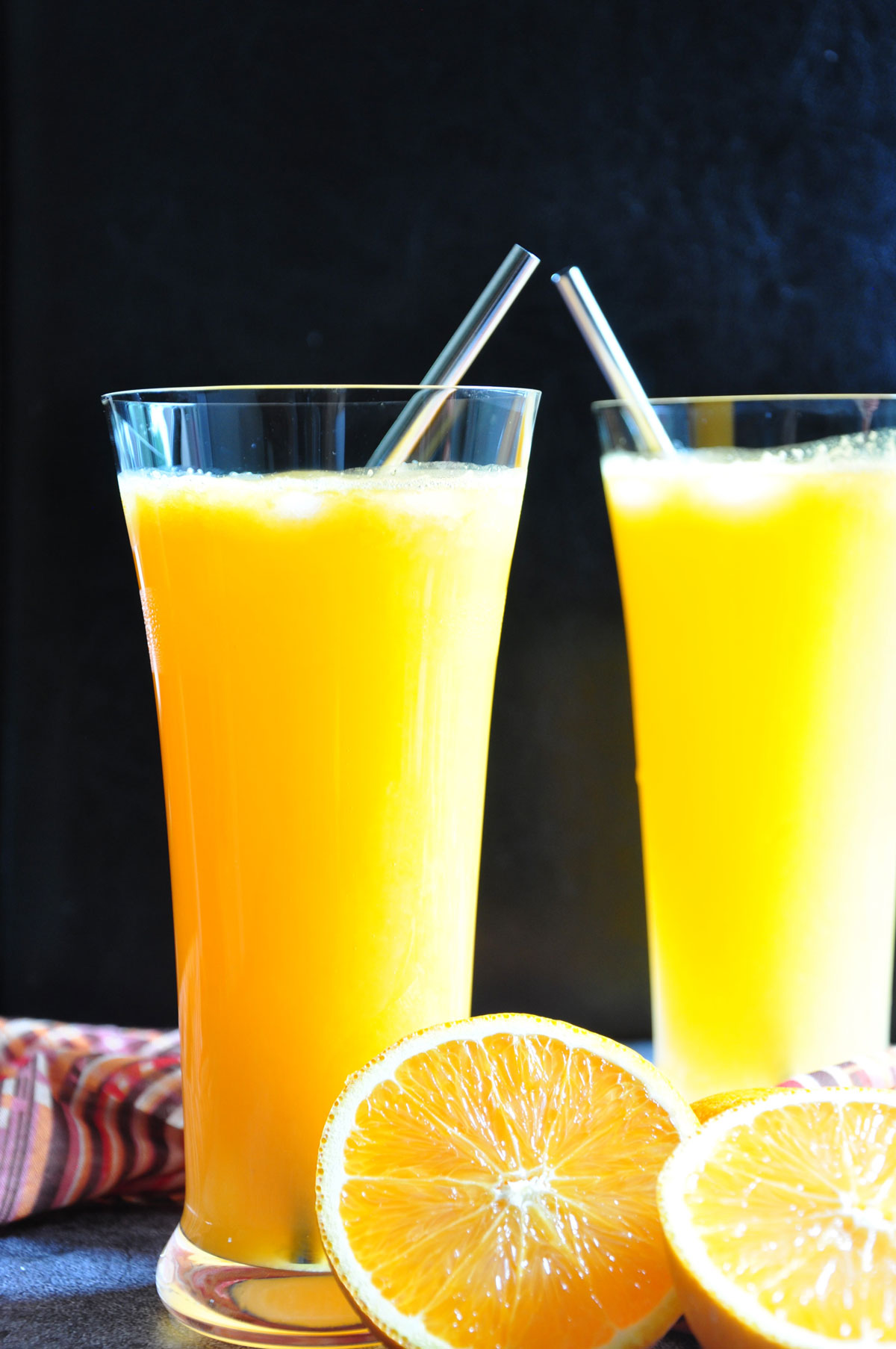 Orange Soda in two tall glass with a cut orange in the foreground.