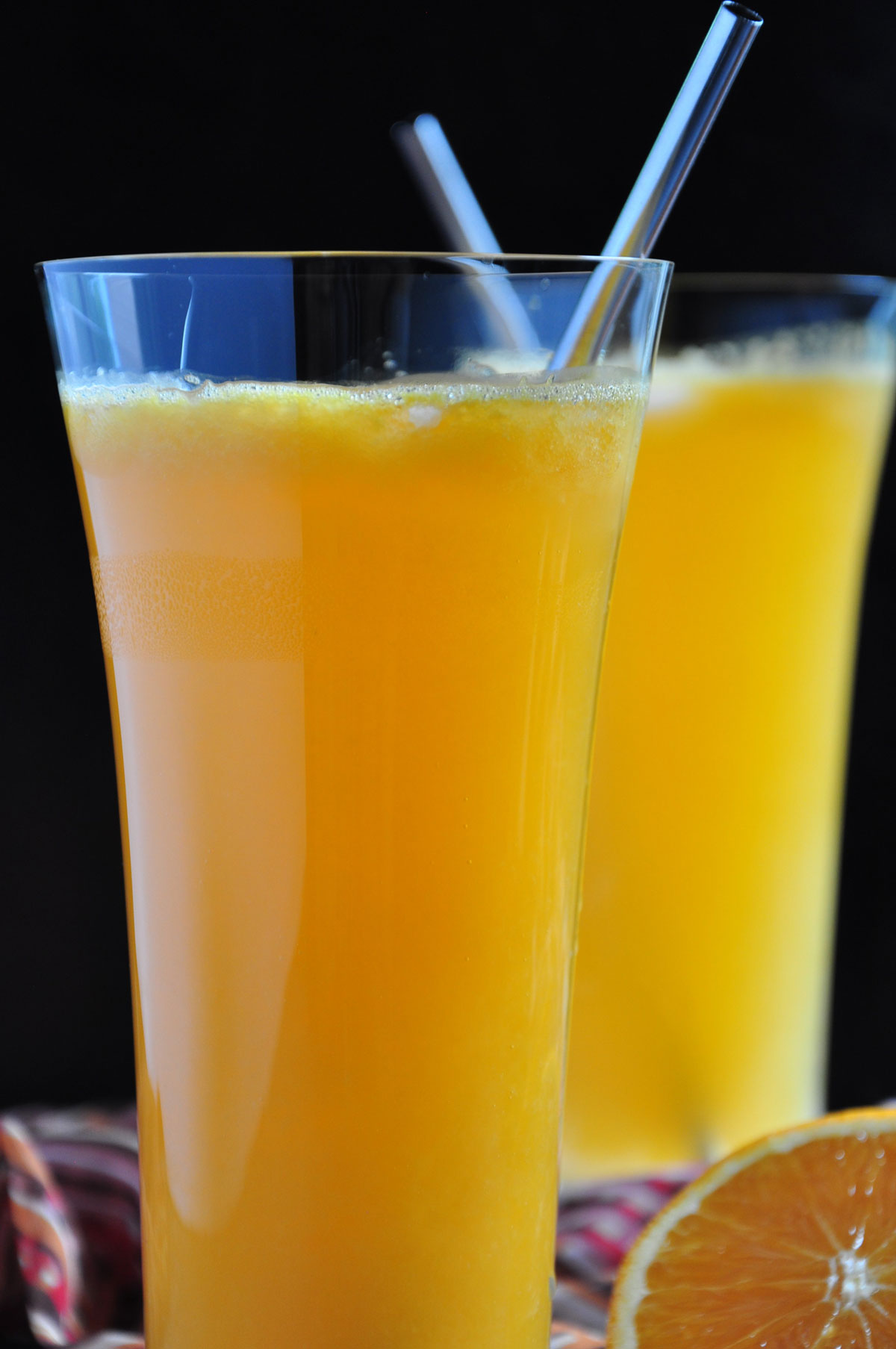 Orange Soda in two tall glass with straws and black background.