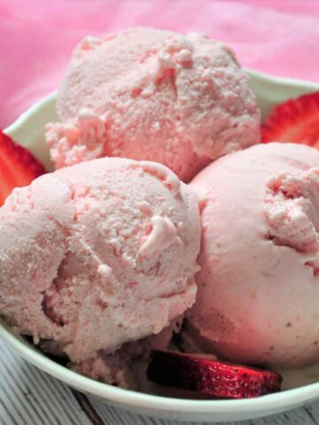 Three scoops of strawberry ice cream with few sliced strawberry a bowl.
