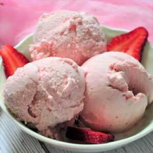 Threeo scoops of strawberry ice cream with few sliced strawberry a bowl.