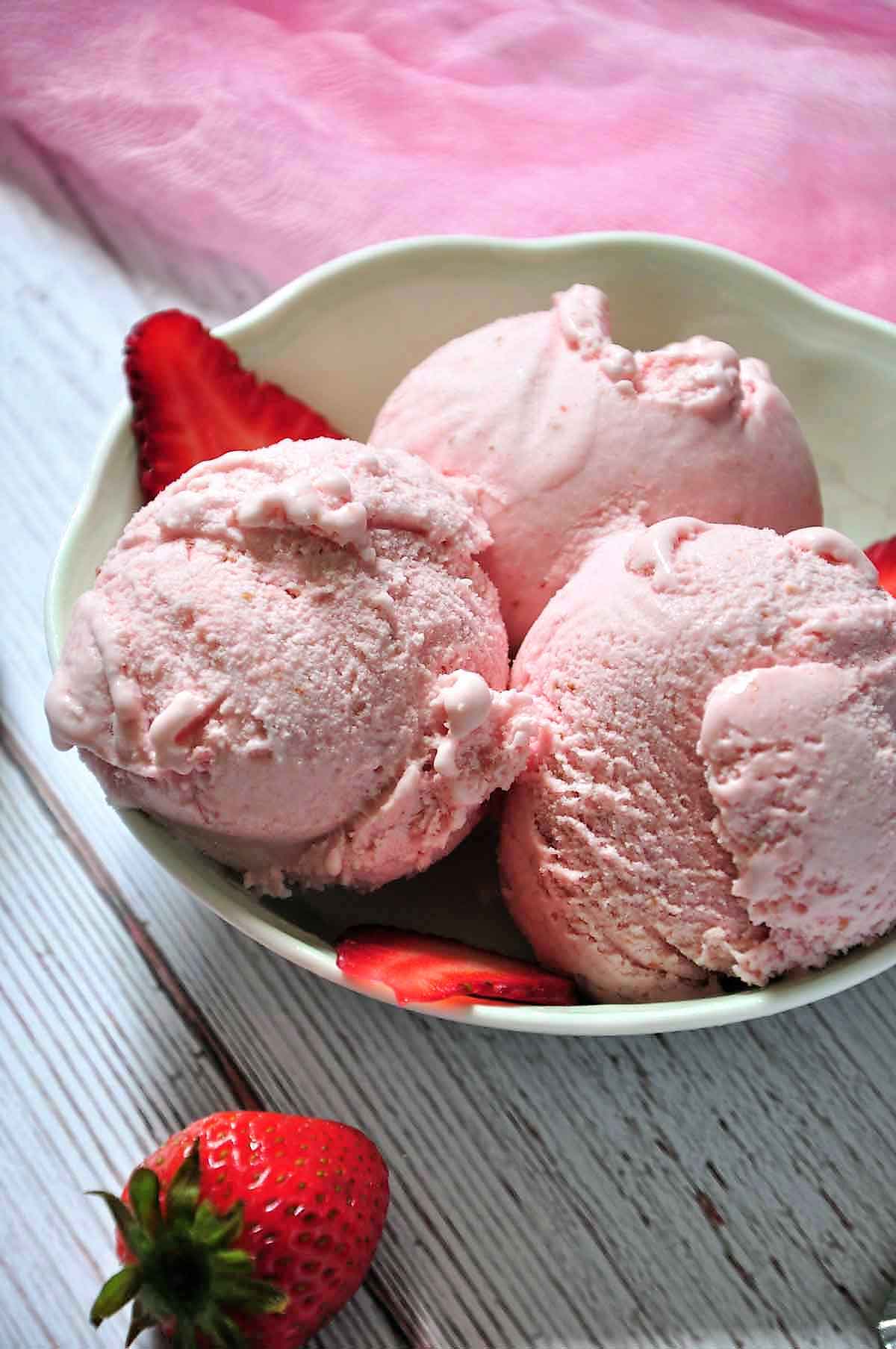 Three scoops of strawberry ice cream in a bowl.