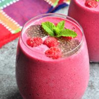mixed berries smoothie in glass garnished with raspberries and chia seeds.