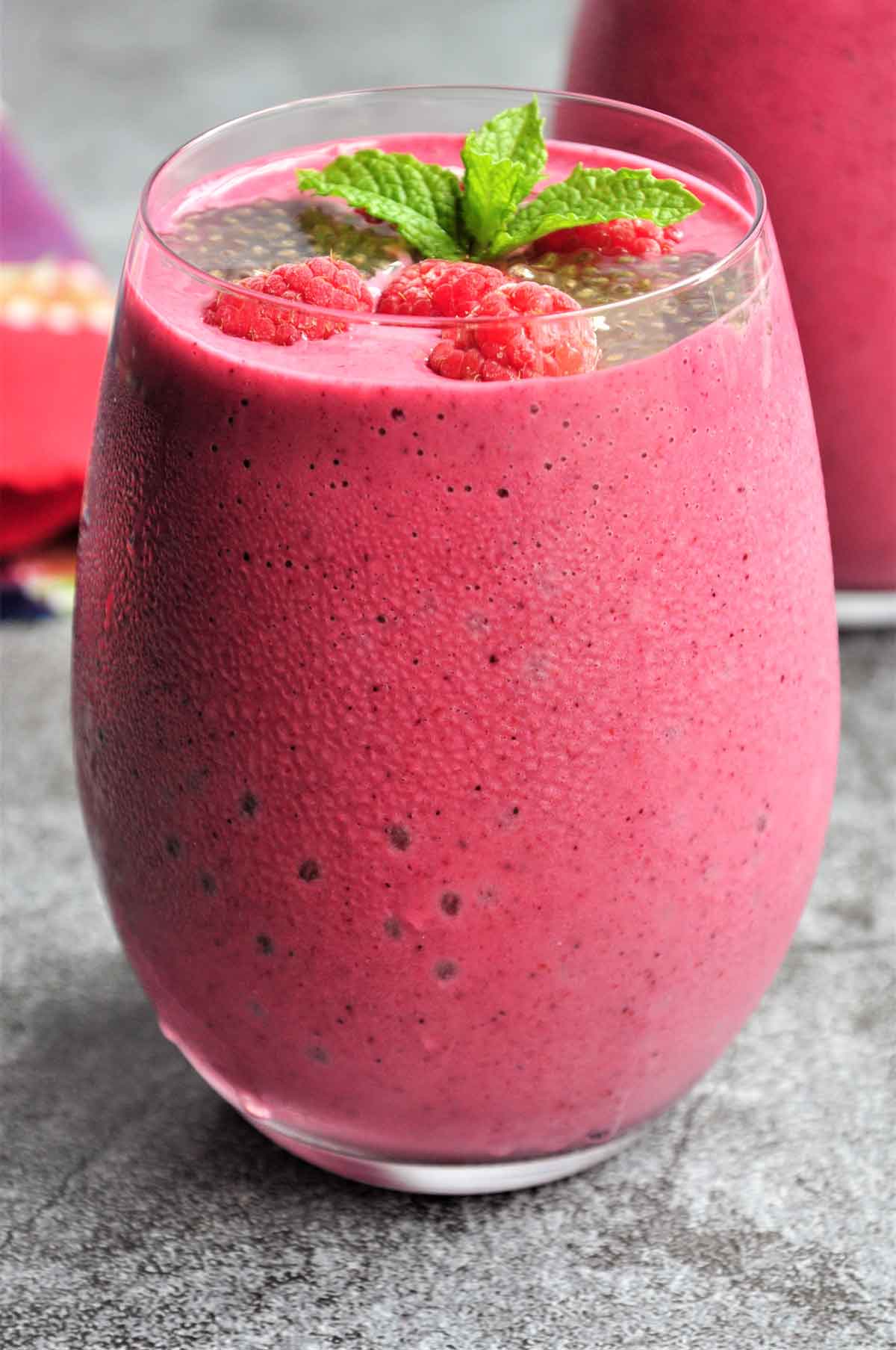 mixed berries smoothie in glass garnished with raspberries and chia seeds.