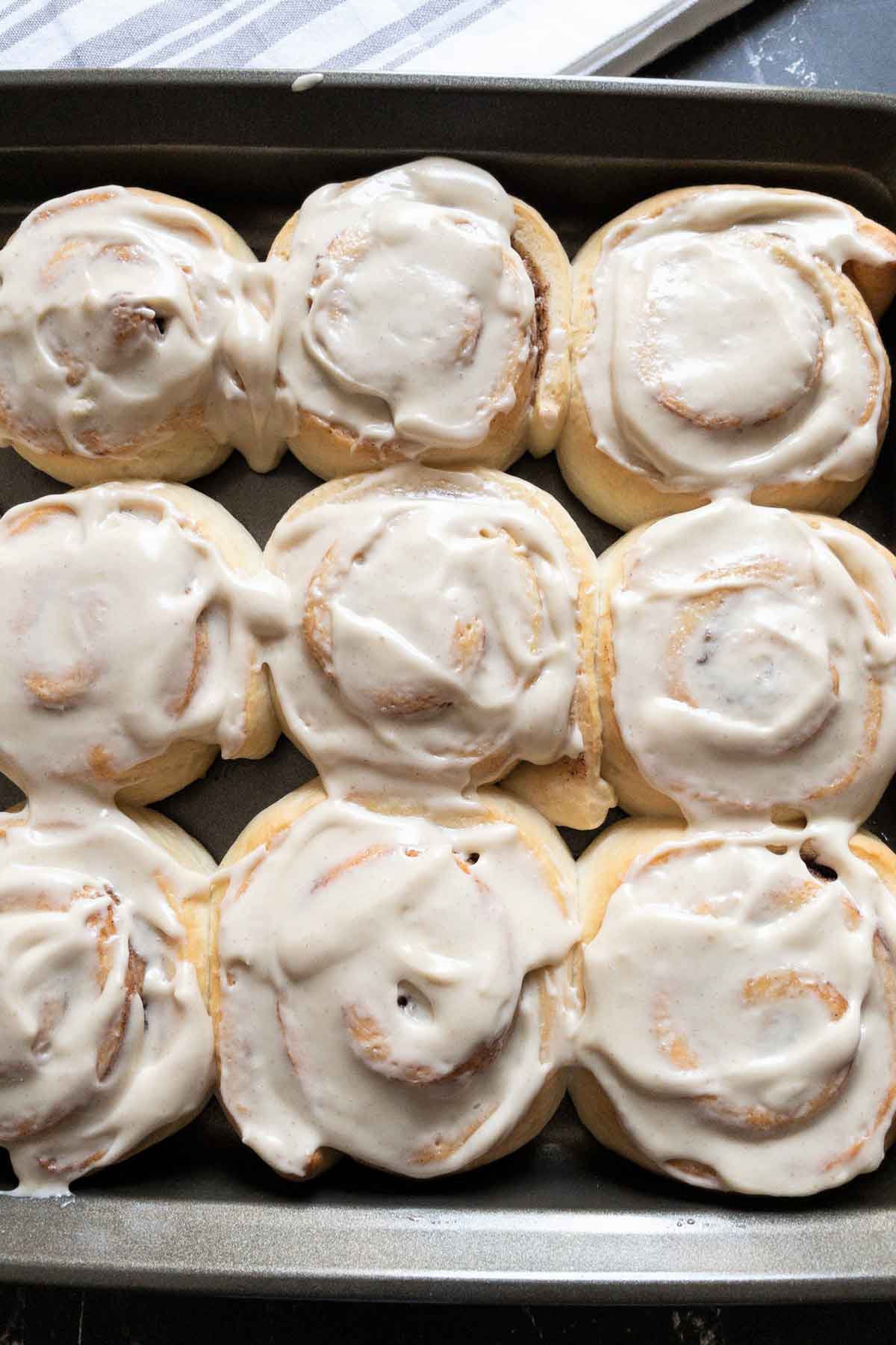 9 cinnamon rolls in a baking tray with icing on top.