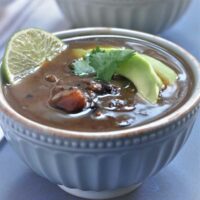 Black Beans Soup in a bowl and garnished with lemon, avacado slice and shredded cheddar cheese.
