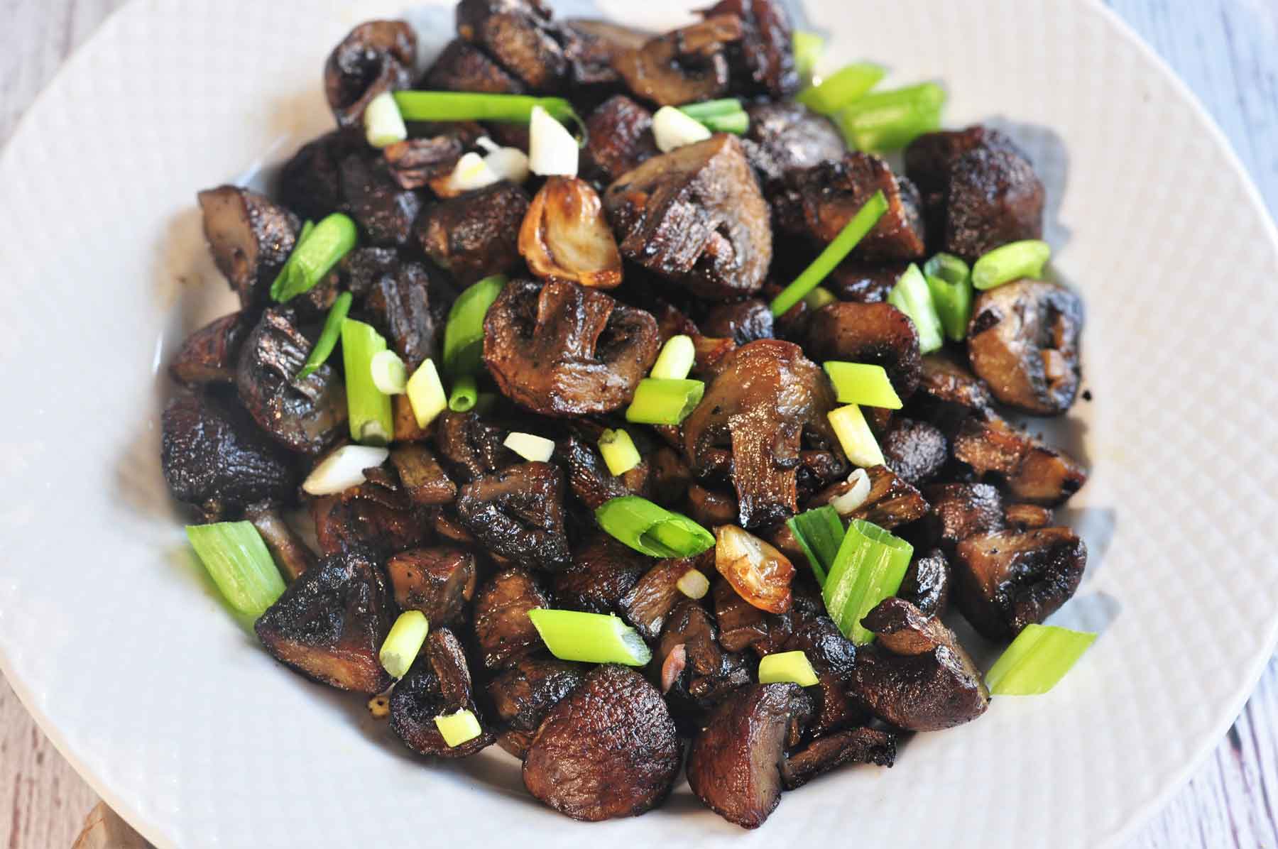 Airfryed mushroom served in a plate and garnished with green onion leaves.
