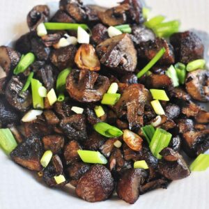 Airfryed mushroom served in a plate and garnished with green onion leaves.