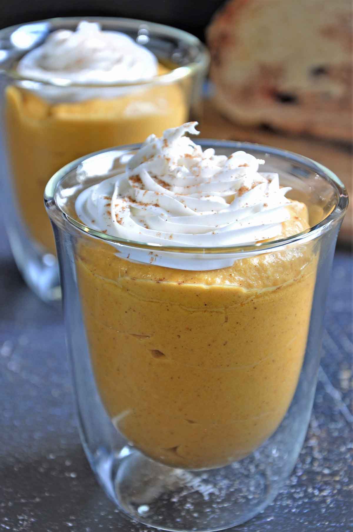 Pumpkin mousse with cream topping in a small serving glass.