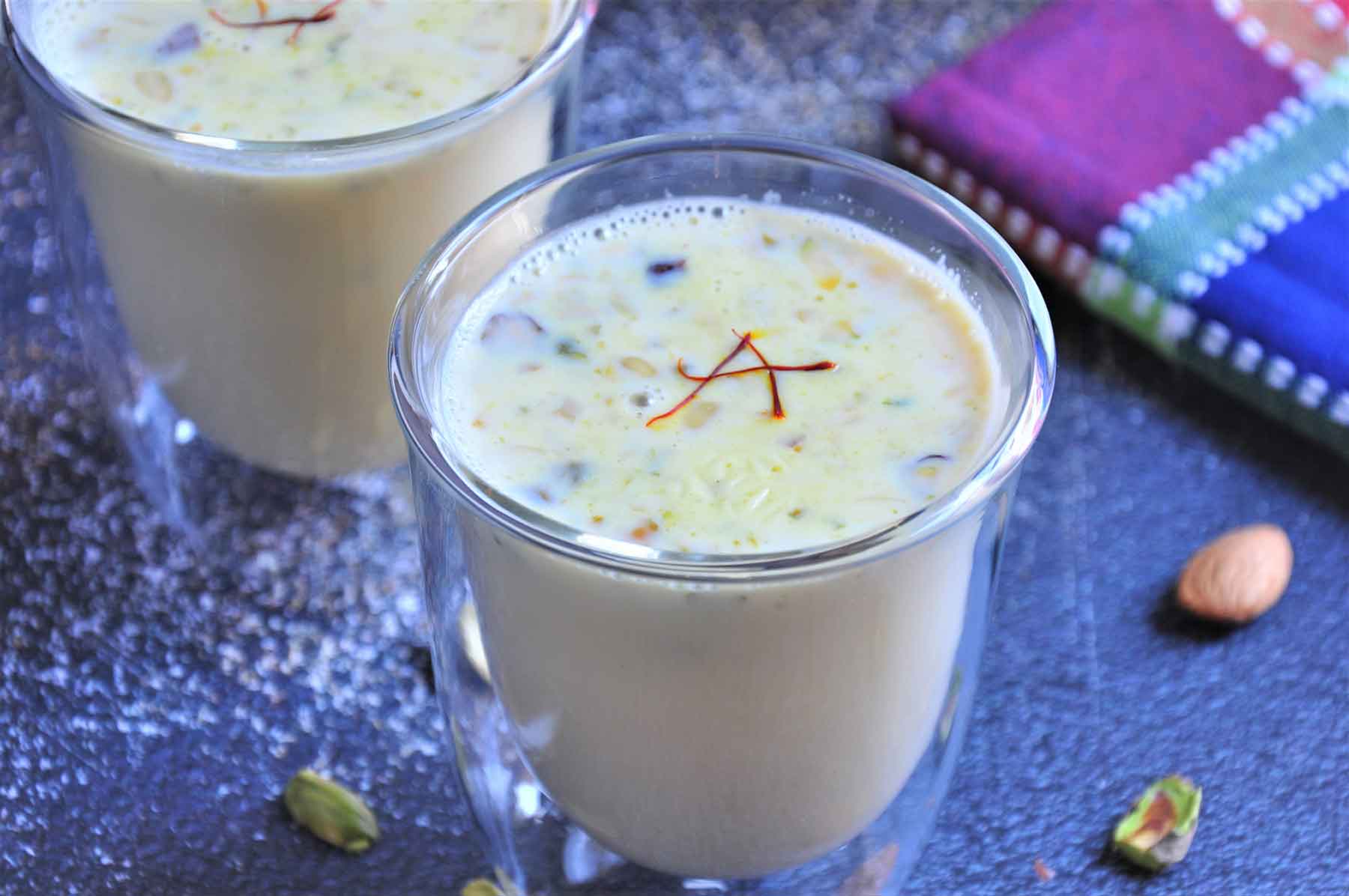 Sweet Almond milk in a glass, garnished with chopped nuts and saffron strands.