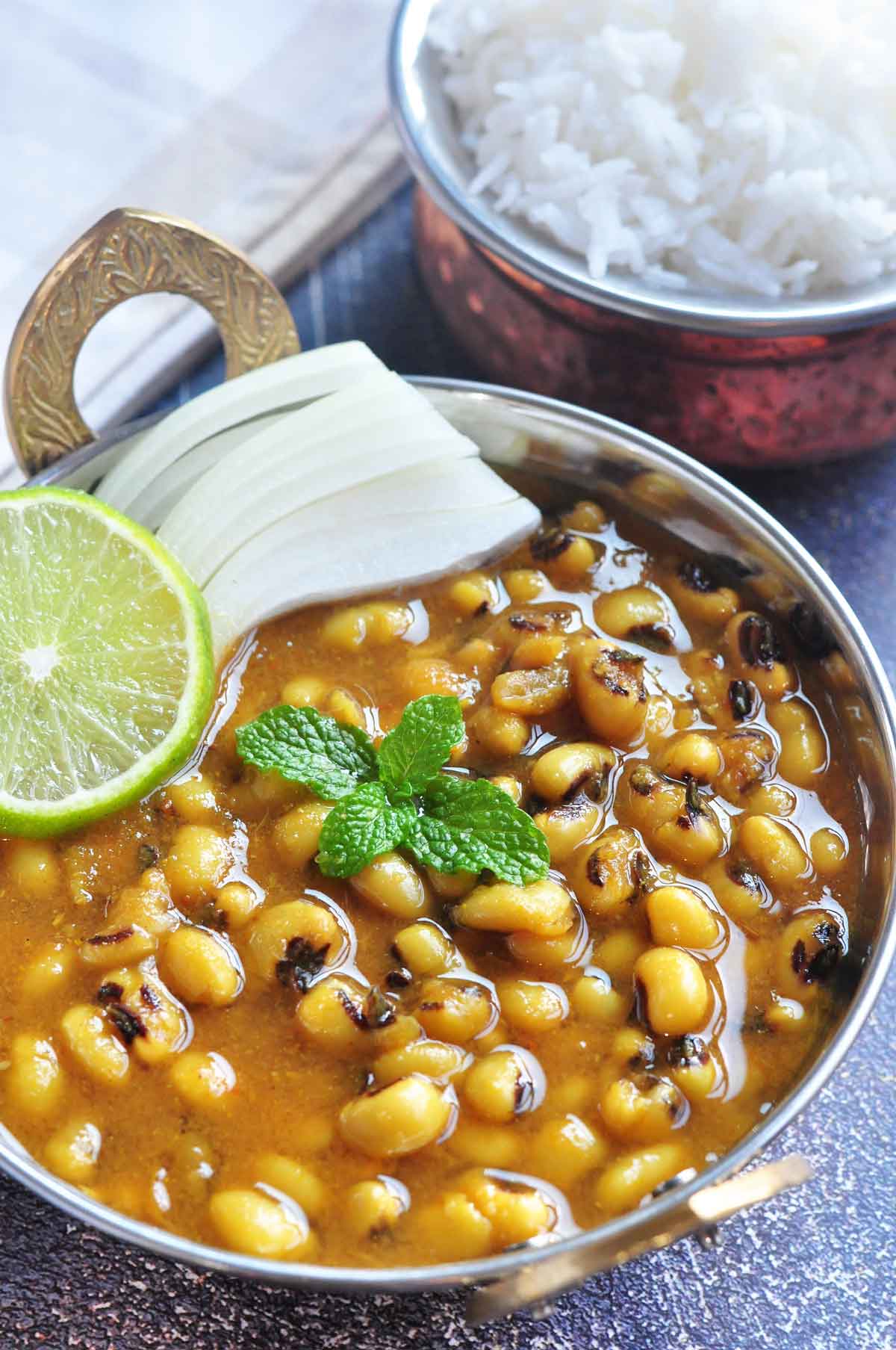 Black eyed pea curry served in a metallic bowl and garnished with sliced lime and onion.