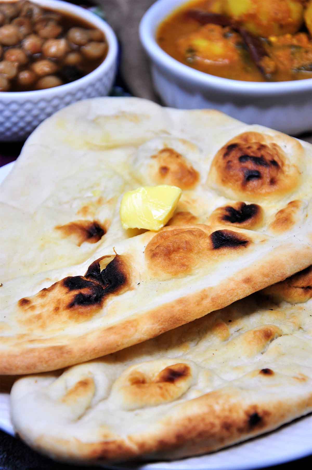Two naans served in a plate with a dollop of butter.