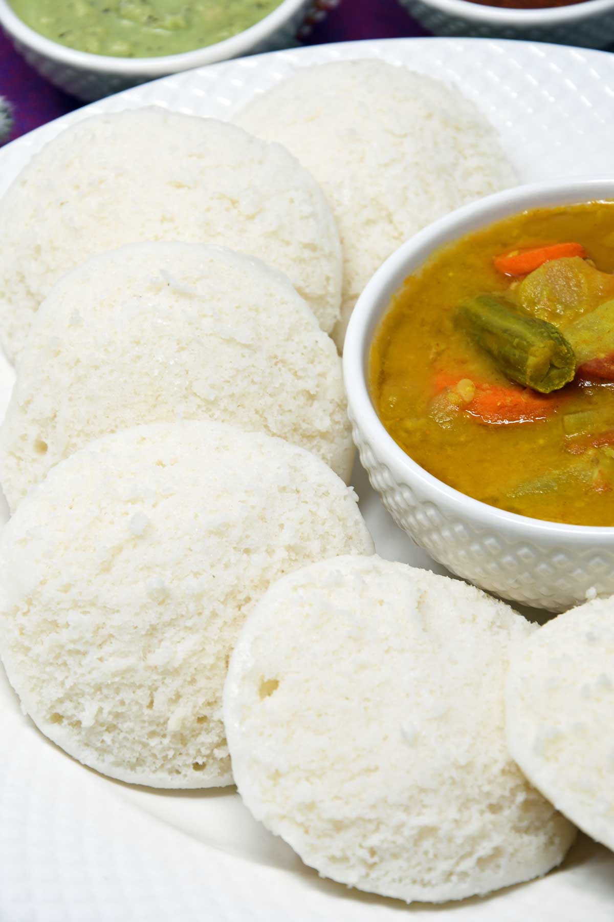 Idlis served in a plate with a bowl of sambhar and chutney.