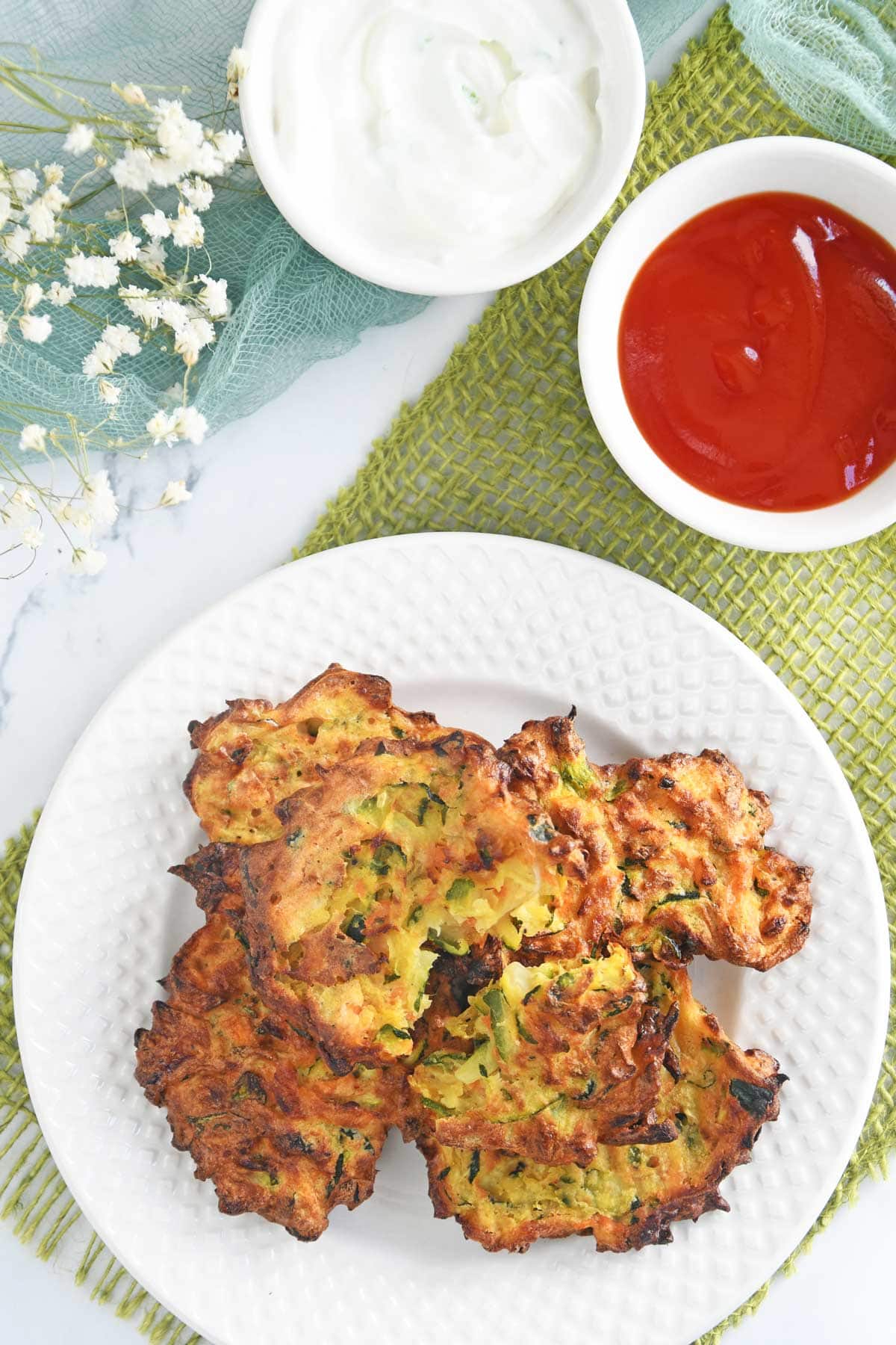 Air fryer Zucchini fritters served in a plate with ketchup and sour cream.