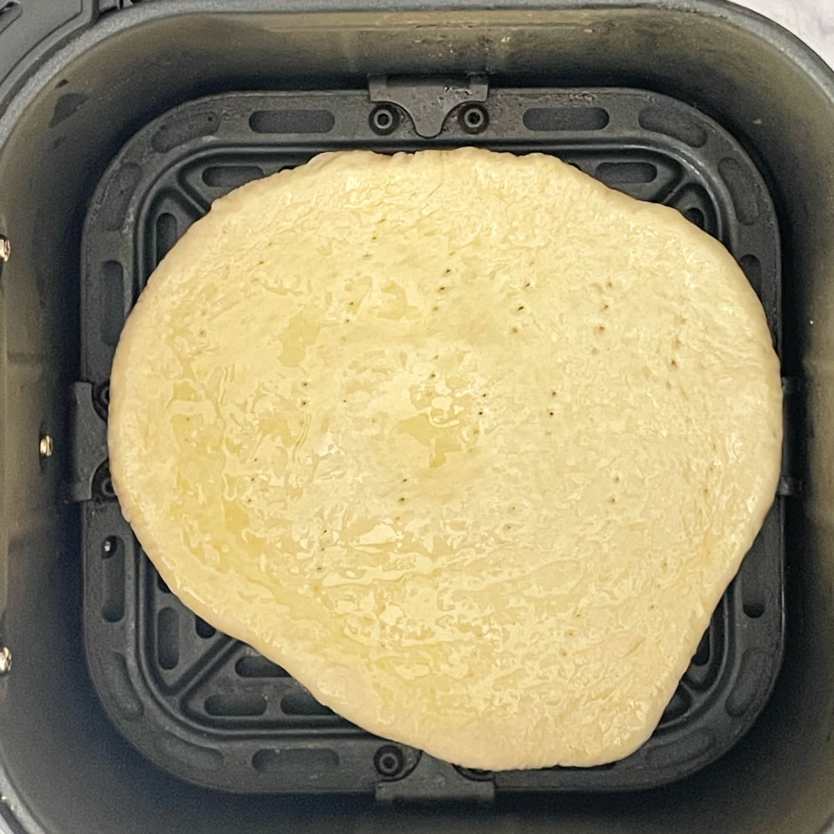 Rolled pizza base in air fryer basket.