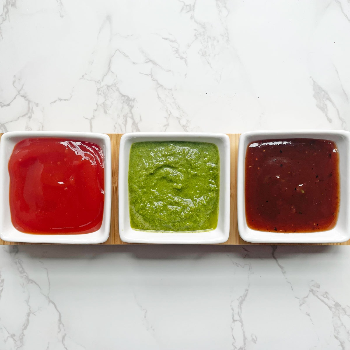 Green chutney, Sweet chutney and sauce in square bowls.